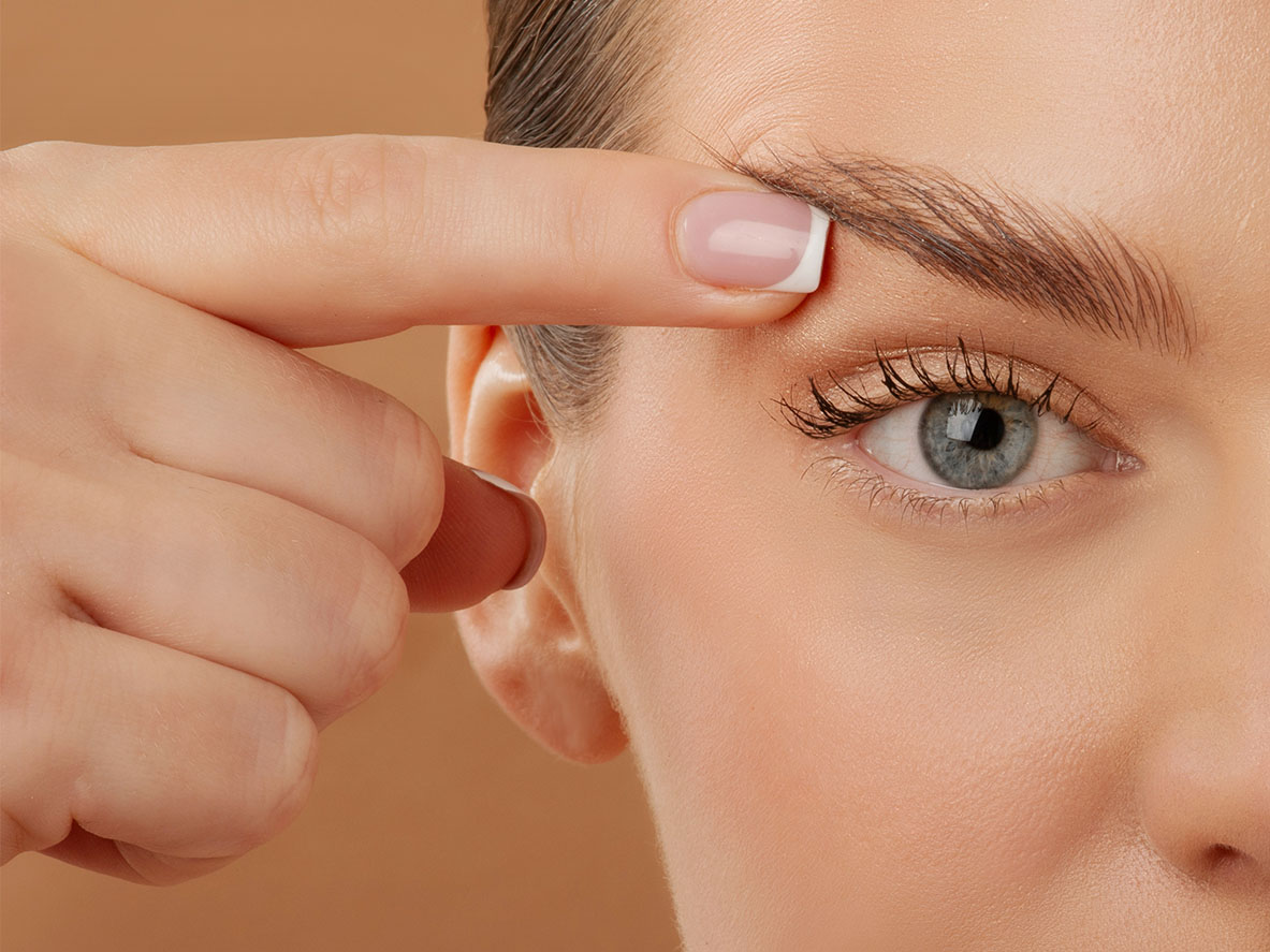 Woman gently lifting her upper eyelid to show the upper eyelid and brow area.