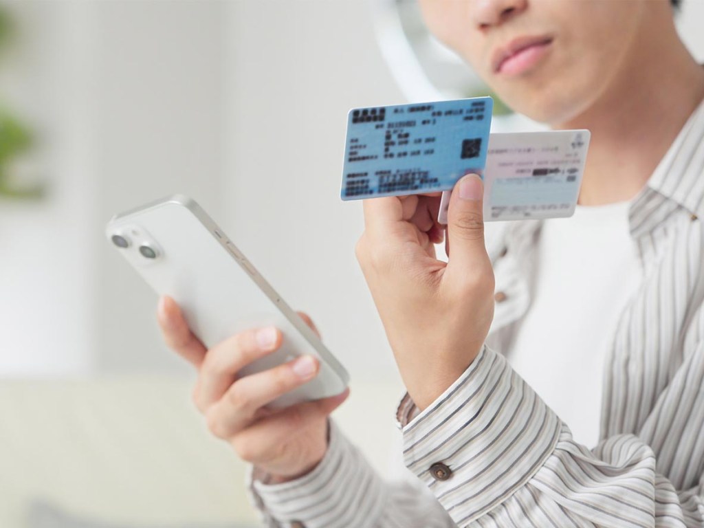 Person holding a smartphone alongside an insurance card and credit card while researching payment options for eyelid surgery, representing insurance coverage and healthcare financing.